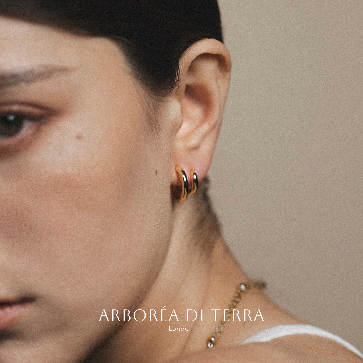 Close-up of an ear wearing a gold hoop earring with 'Arboréa di Terra' branding.