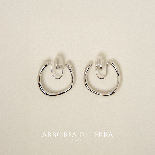Pair of silver hoop earrings on a beige background with 'Arboréa di Terra' branding.