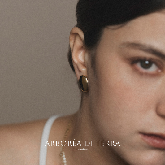 Close-up of a person wearing gold earrings with 'Arboréa di Terra' branding.
