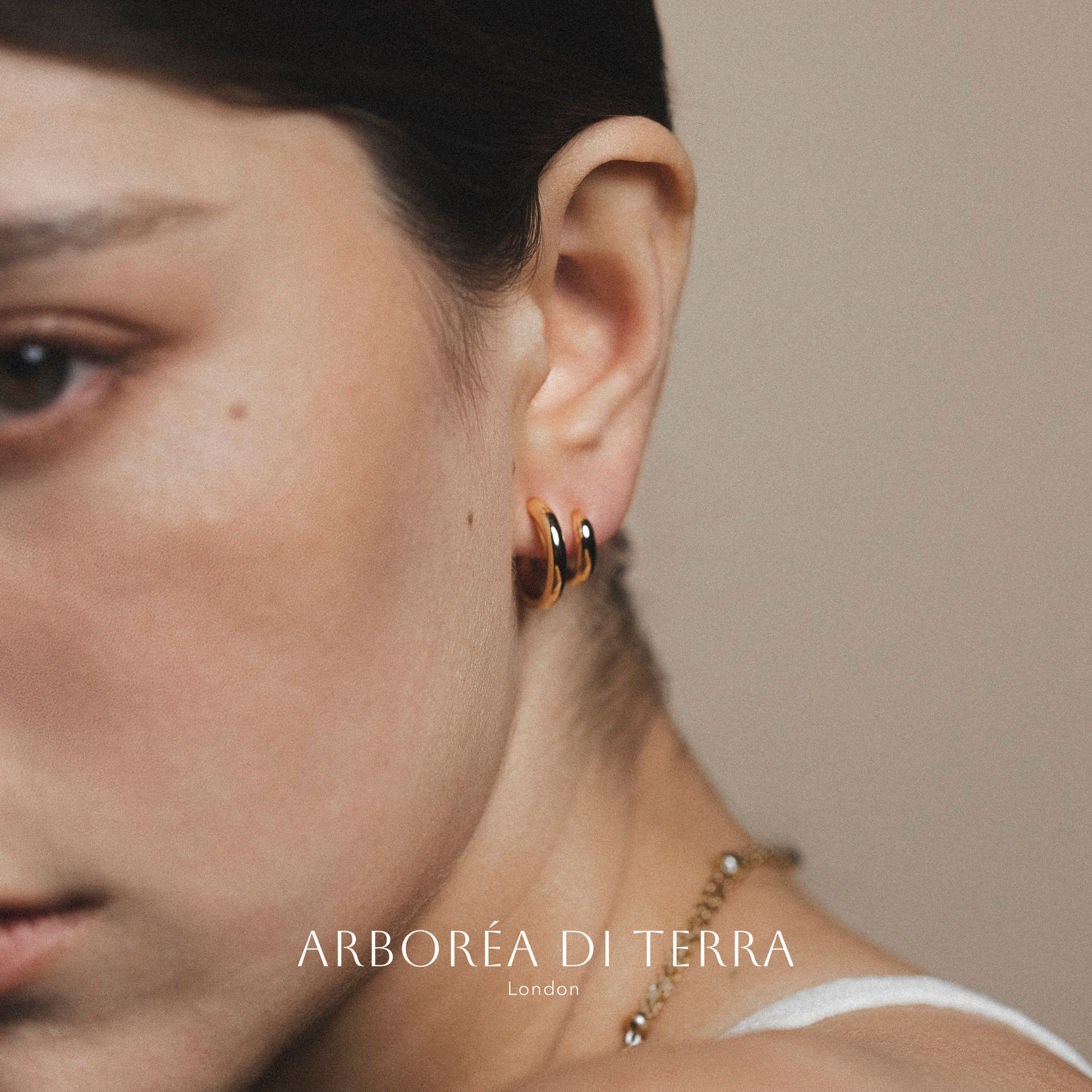 Close-up of an ear wearing a gold hoop earring with 'Arboréa di Terra' branding.