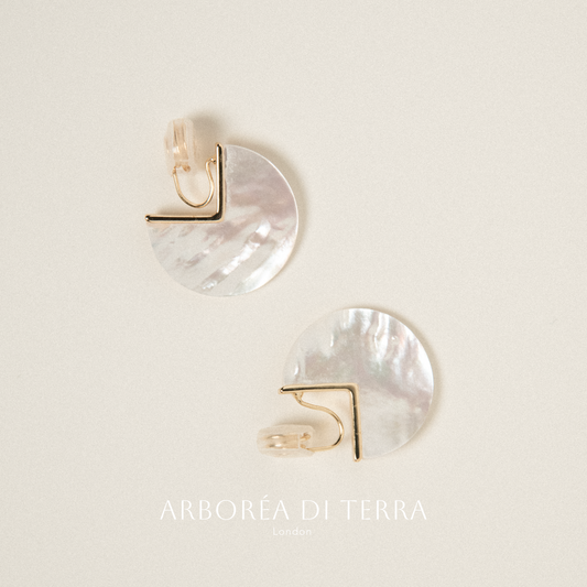 Pair of earrings with gold and white half-circle design on a light background, branded 'Arborea di Terra'.