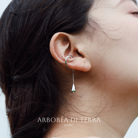Close-up of an ear wearing a silver earring with 'Arboréa di Terra' branding.