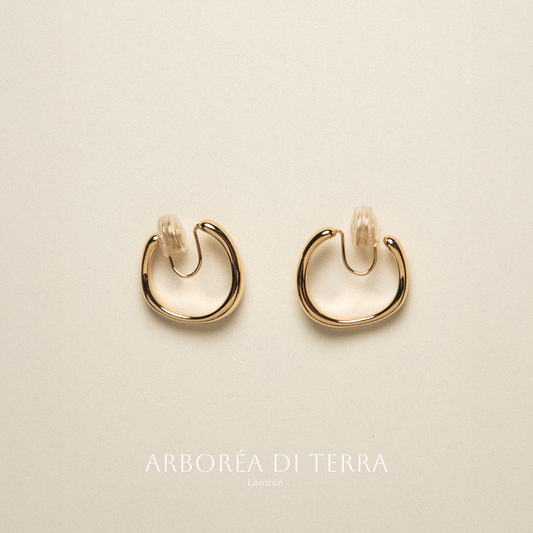 Gold hoop earrings on a beige background with 'Arborea Di Terra' branding.