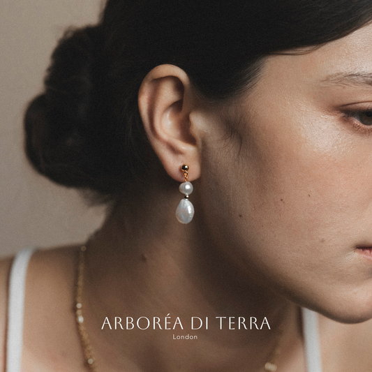 Close-up of a woman wearing pearl earrings with 'Arboréa di Terra' branding.