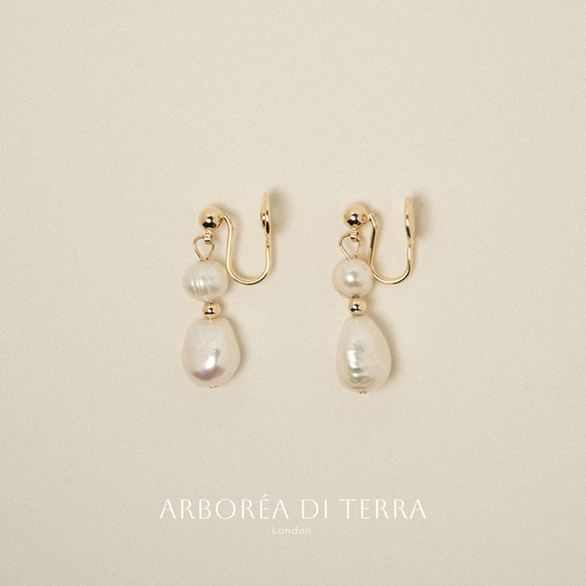 Pair of pearl earrings with gold hooks on a beige background, branded 'Arboréa di Terra'.