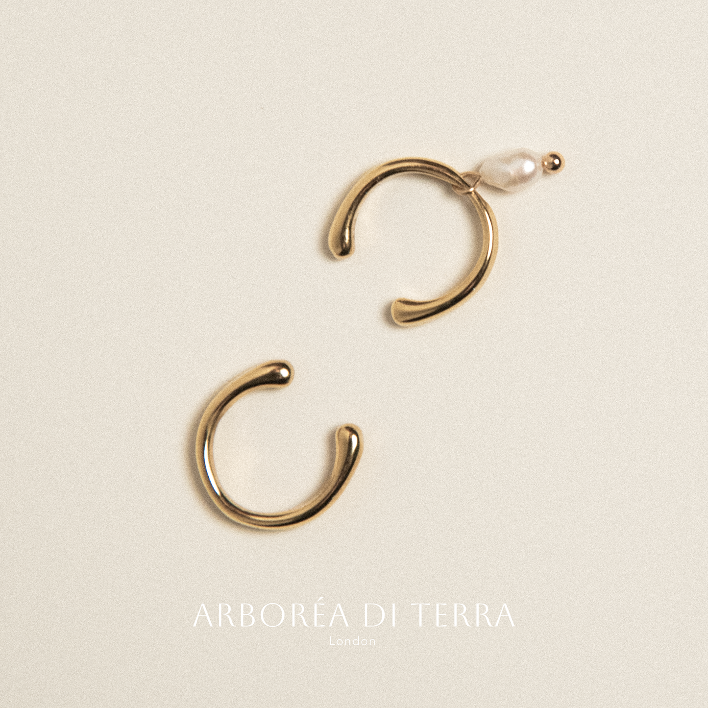 Gold hoop earrings with a pearl on a beige background, featuring the brand 'Arborea di Terra'.