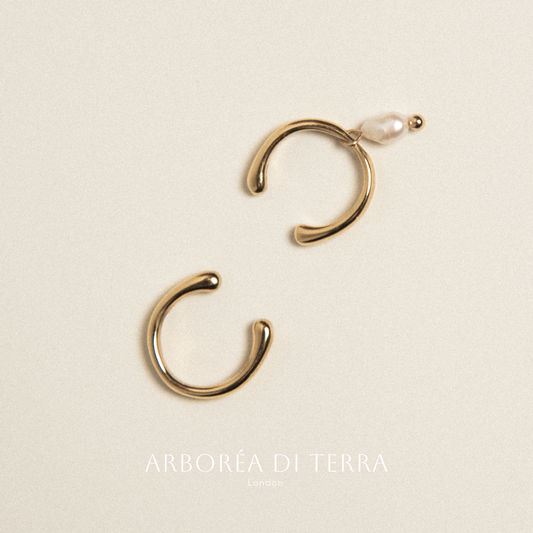 Gold hoop earrings with a pearl on a beige background, featuring the brand 'Arborea di Terra'.